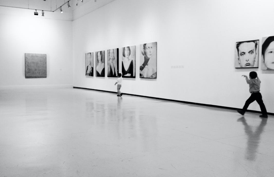 Visitors viewing framed portrait works hung along a gallery wall